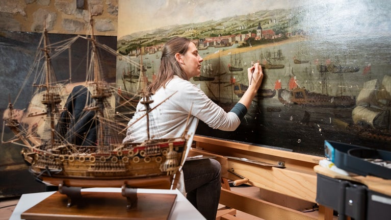 A conservator working on ‘A View of the Port of Bridgetown, Barbados’ painting at the Royal Oak Foundation Studio